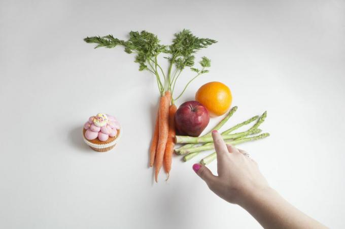 en hånd strekker seg etter et utvalg av frukt og grønnsaker i stedet for en cupcake