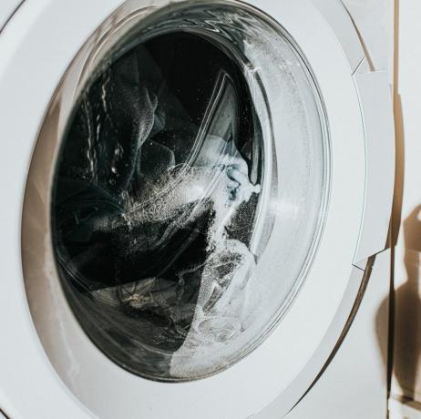 nærbilde på en hvit vaskemaskin med glassfront, mens klærne snurrer rundt midt i syklusen kaster glasset en skygge på veggen, med plass til kopi