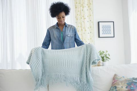 African American woman folding teppe på sofaen