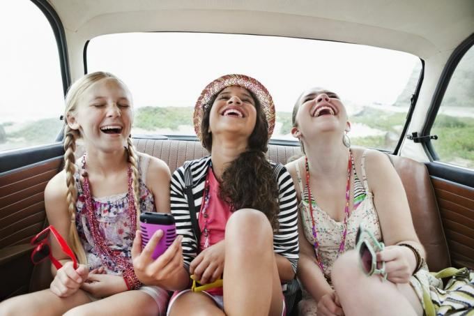 tre jenter som ler i baksetet på et kjøretøy
