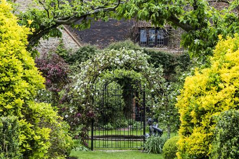 hage med busker og lysthus med blomstrende planter om våren, hytte i bakgrunnen