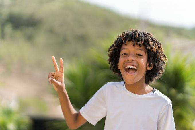 10 år gammel afroamerikansk gutt som ler høyt mens han lager fredstegn
