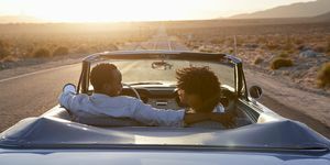 bakfra av par på biltur som kjører klassisk kabriolet bil mot solnedgang