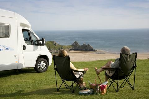 Et par med en piknik slapper av i stolene sine ved siden av sin bobil og nyter utsikten over Three Cliffs Bay på Gower-halvøya i Wales., Three Cliffs Bay, Swansea, Wales.