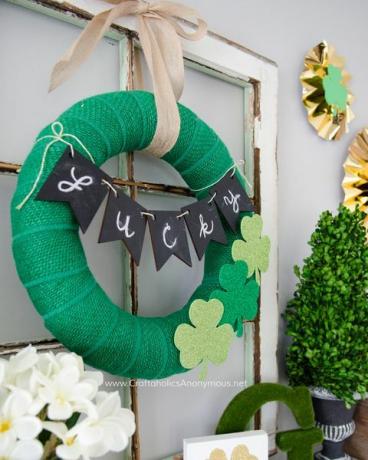 grønn burlapkrans med tre glitrende skumkramper og et "heldig" banner bundet over den henger på en vinduskarm som sitter på en mantel