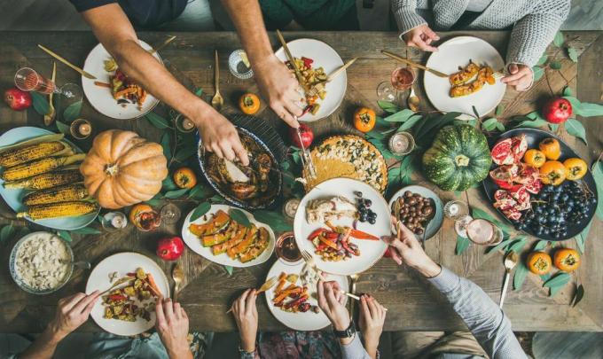 ovenfra av Thanksgiving Day-bordet med kalkun, gresskarpai, stekte sesongens grønnsaker og frukt og folk som fyller tallerkener og spiser