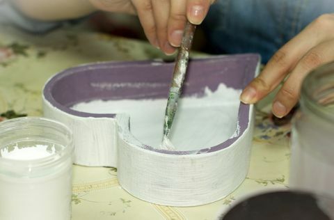 hender som maler innsiden av en lilla treformet kasse hvit
