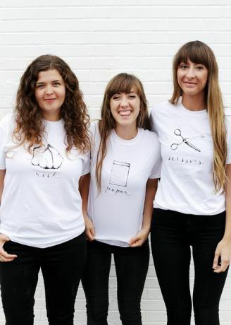 tre kvinner i hvite t-skjorter, med enten stein, papir eller saks skrevet og avbildet på skjorten