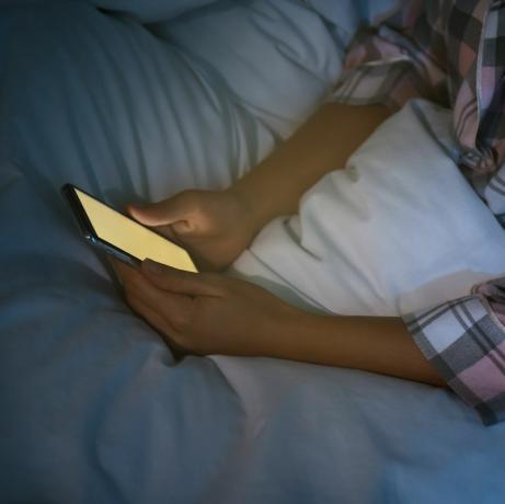 kvinne som bruker smarttelefon i sengen om natten, nærbilde nomofobi og søvnforstyrrelsesproblem
