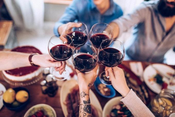 hender og armer på fem personer som skåler med glass med vin over et middagsbord