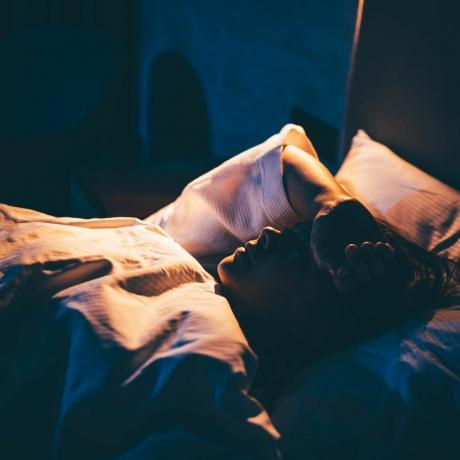 kvinne med søvnløshet ung kvinne liggende på sengen med hånden på pannen