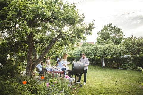 mannlige og kvinnelige venner som tilbereder mat på grillen mens familien har det moro i hagen