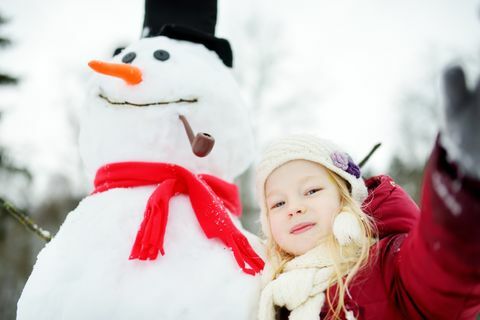 Bedårende liten jente som bygger en snømann i vakker vinterpark. Søtt barn som leker i en snø.