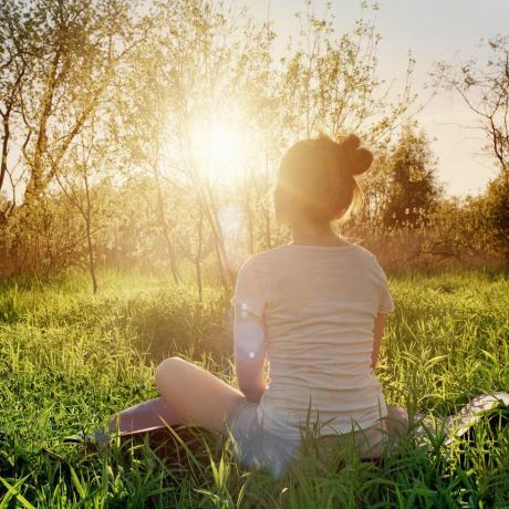 ung kvinne som sitter i yogastilling og nyter solnedgangen i naturen