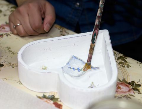 en håndverkerhånd som maler et utskåret bilde med lim på innsiden av en hvit, hjerteformet boks