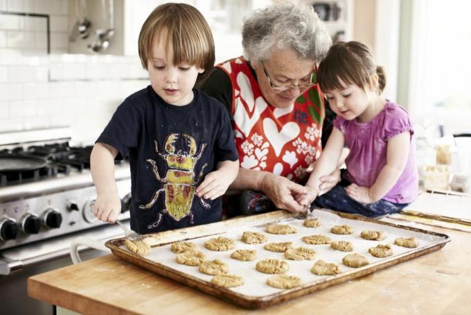 bestemor og to små barnebarn som baker barnebarnet legger deig på et kakeark med bestemødres hjelp