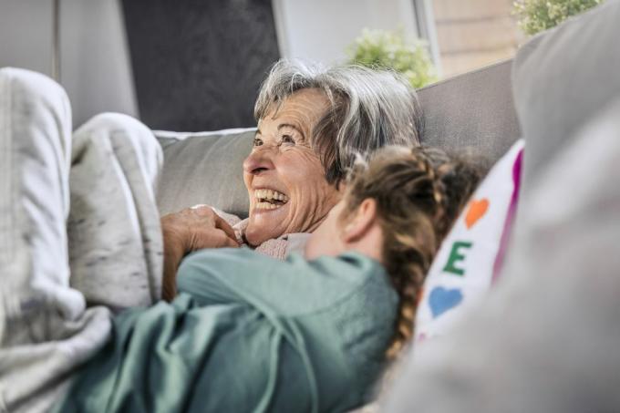 blid bestemor som ligger ved barnebarnet på sofaen hjemme